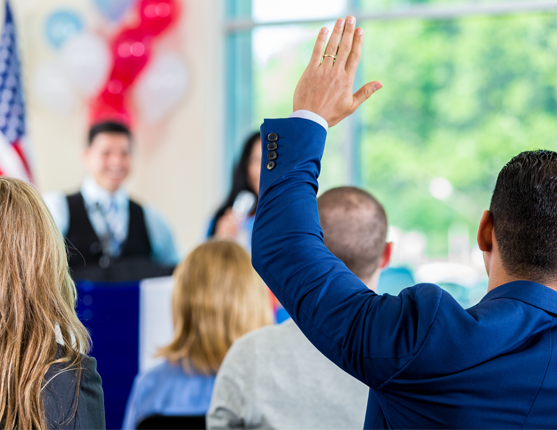 Image: Speaker with audience with hands raised