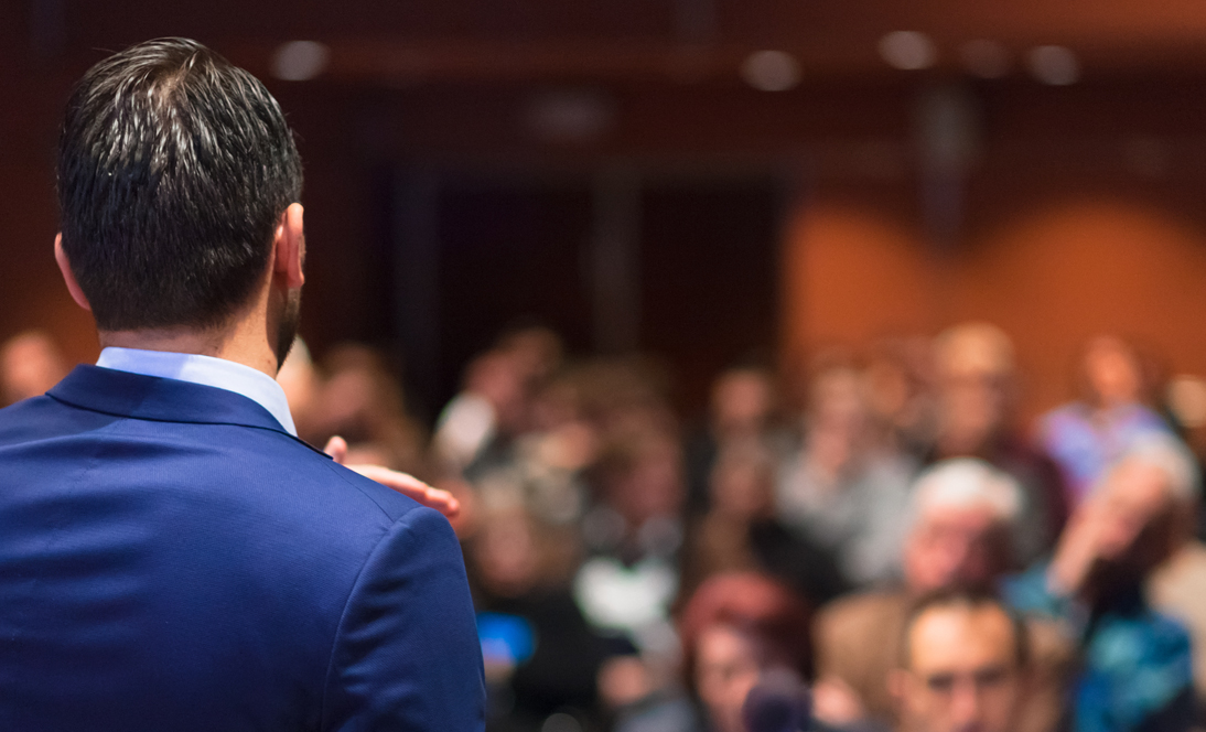 Image: back of man presenting to audience at meeting