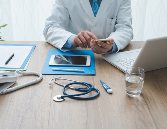 Image: Doctor at desk with computer tablet and phone